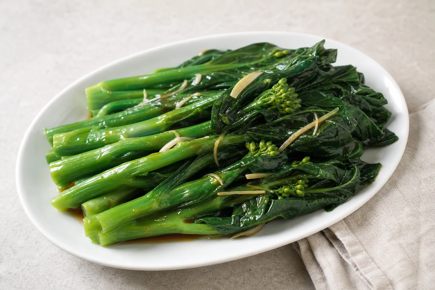 Blanched gai lan with oyster sauce on a white oval plate.