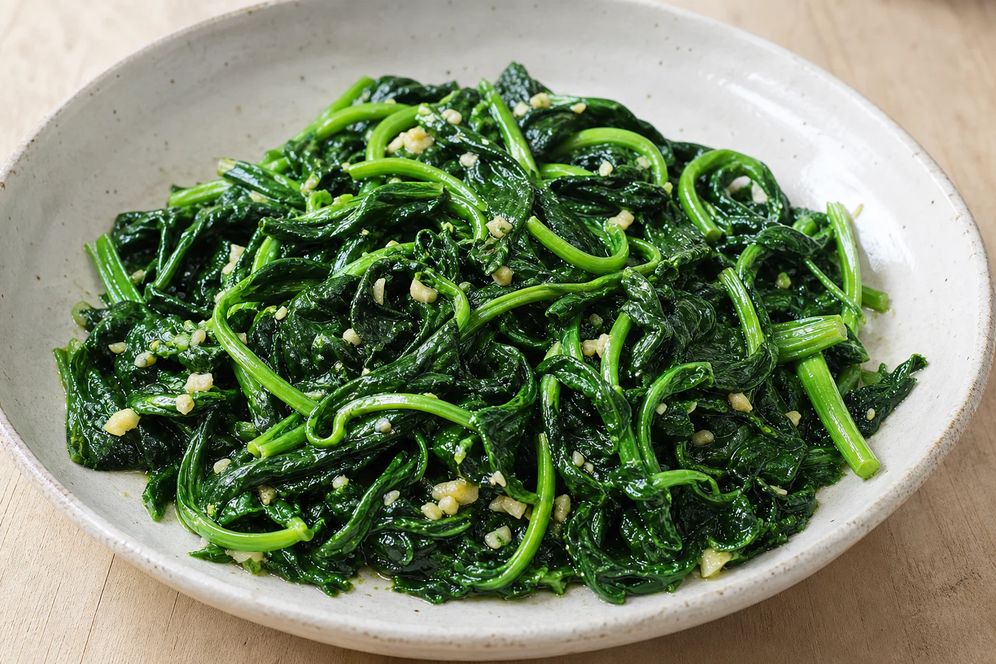 Garlic stir-fried snow pea tips in a shallow ceramic bowl.